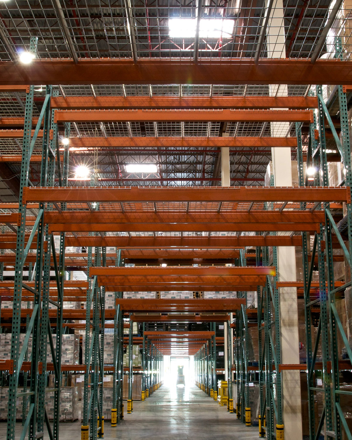 Tall pallet racking lining the aisle of a warehouse lit by overhead high bay fixtures